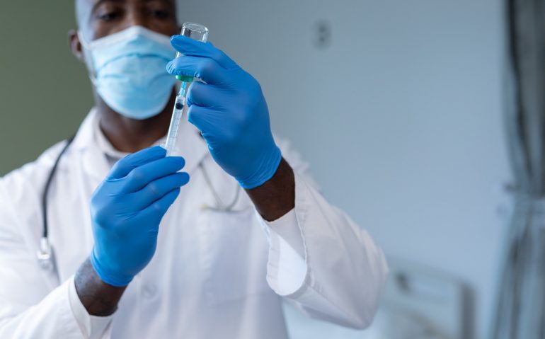 African american male doctor wearing face mask and gloves preparing covid vaccination