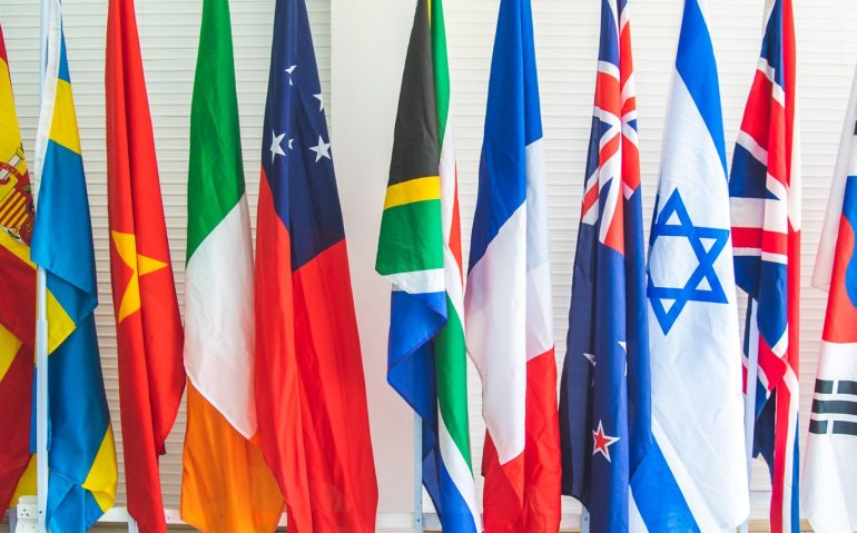 collection of various flags of different countries standing tall together in a row on a stand