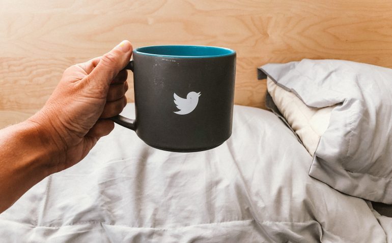 Hand holding mug with a tweeter bird sign